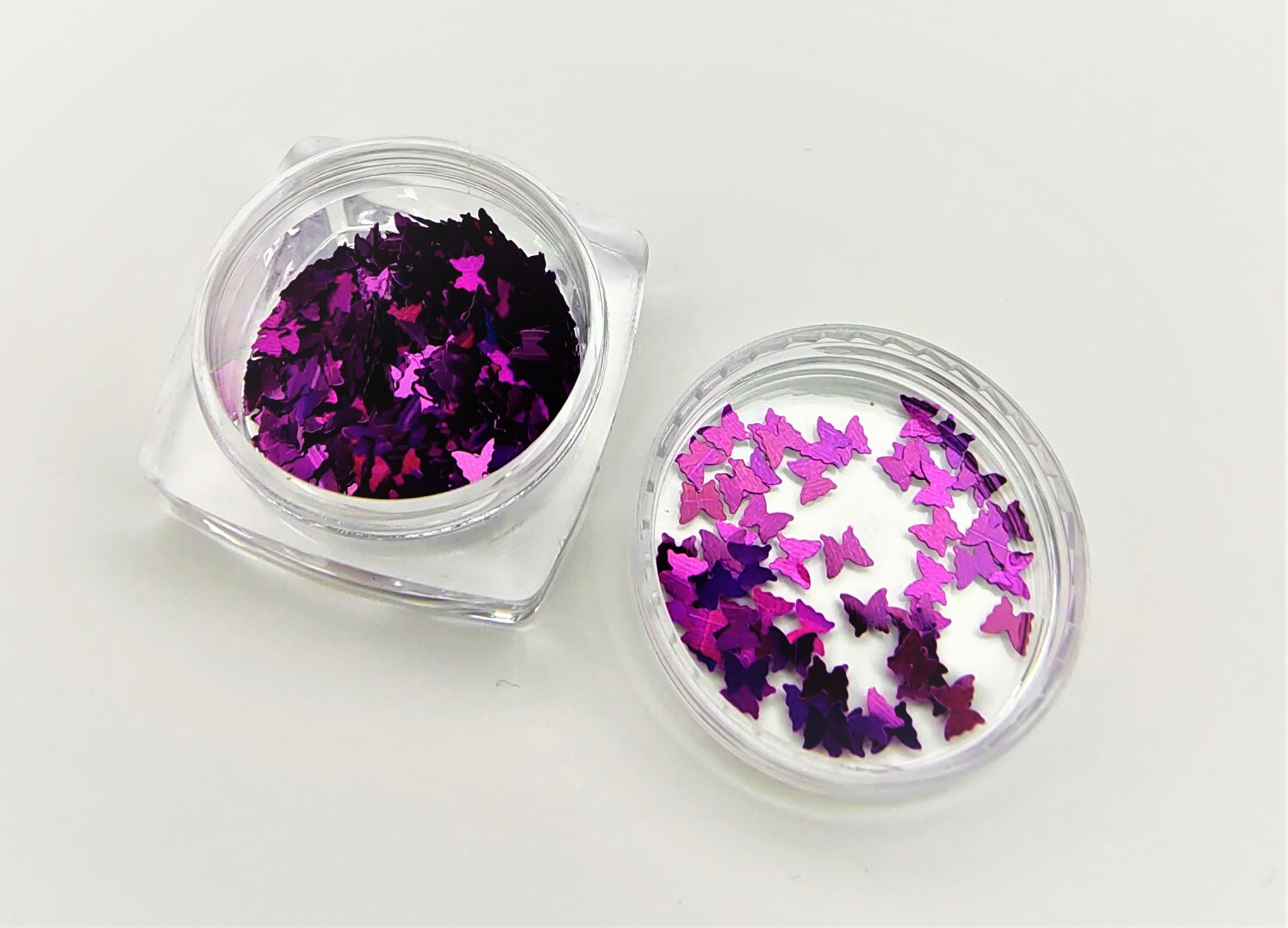 Dois pequenos recipientes com glitter em forma de borboletas roxas e rosa