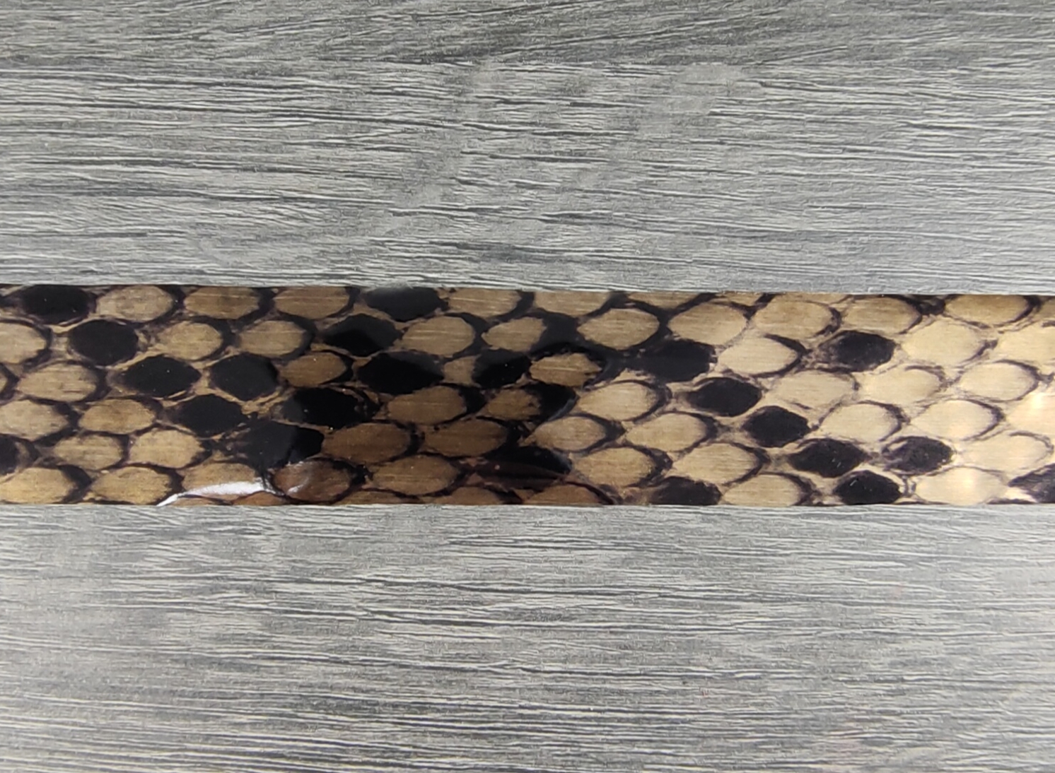 Tira com padrão de escamas de cobra castanho e preto sobre madeira cinza