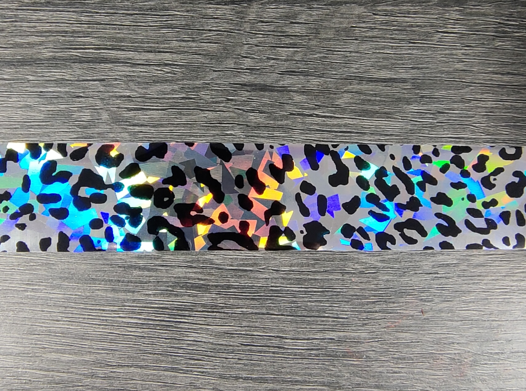 Fita adesiva holográfica com padrão de manchas pretas sobre fundo prateado