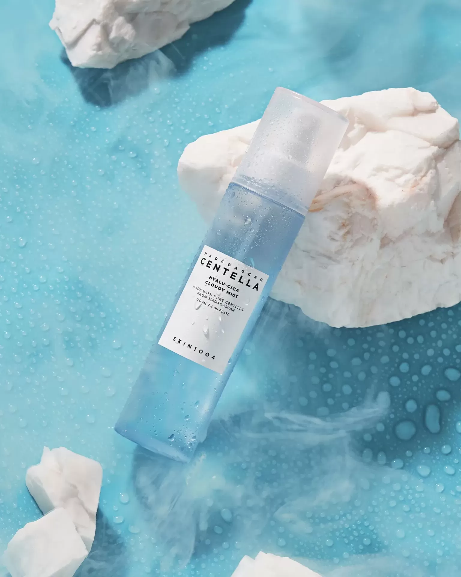 Frasco azul claro de toner cosmético SKINFOOD sobre superfície azul com gotas de água e pedras brancas