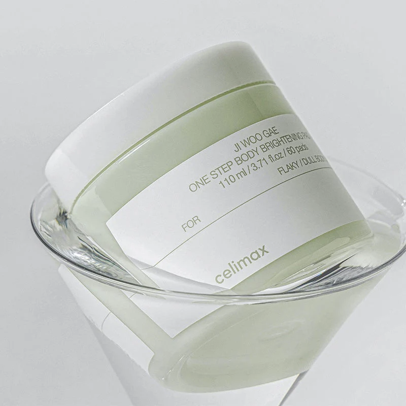 Frasco de creme corporal verde com tampa branca e rótulo branco inclinado numa taça de vidro.