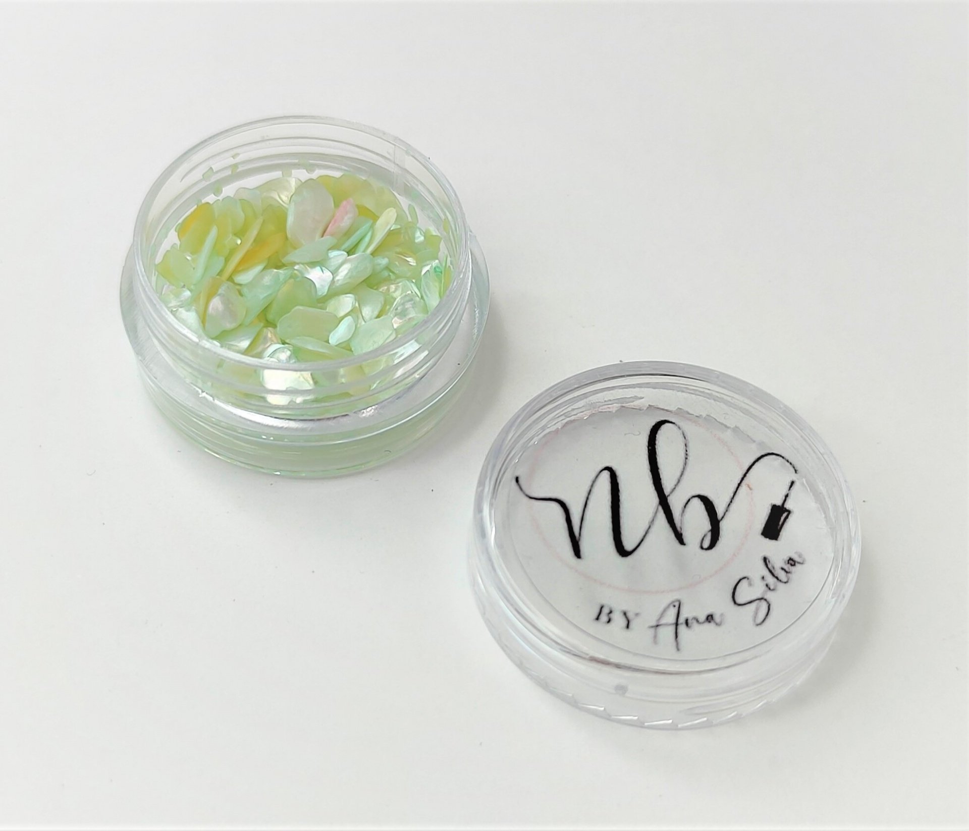 Frasco pequeno transparente com pedaços coloridos e tampa com texto.