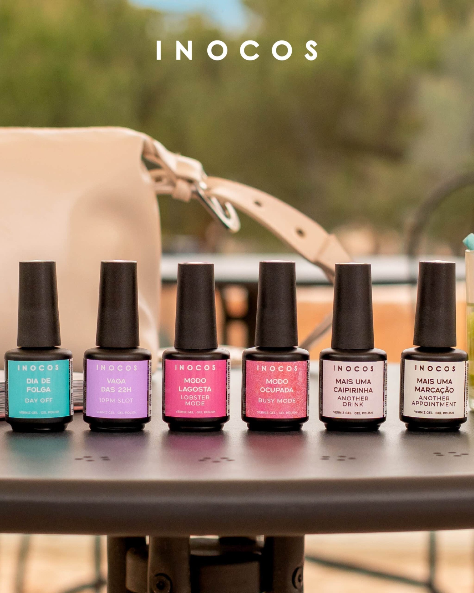 Seis frascos de verniz gel com rótulos coloridos e texto INOCOS sobre mesa preta com bolsa bege ao fundo