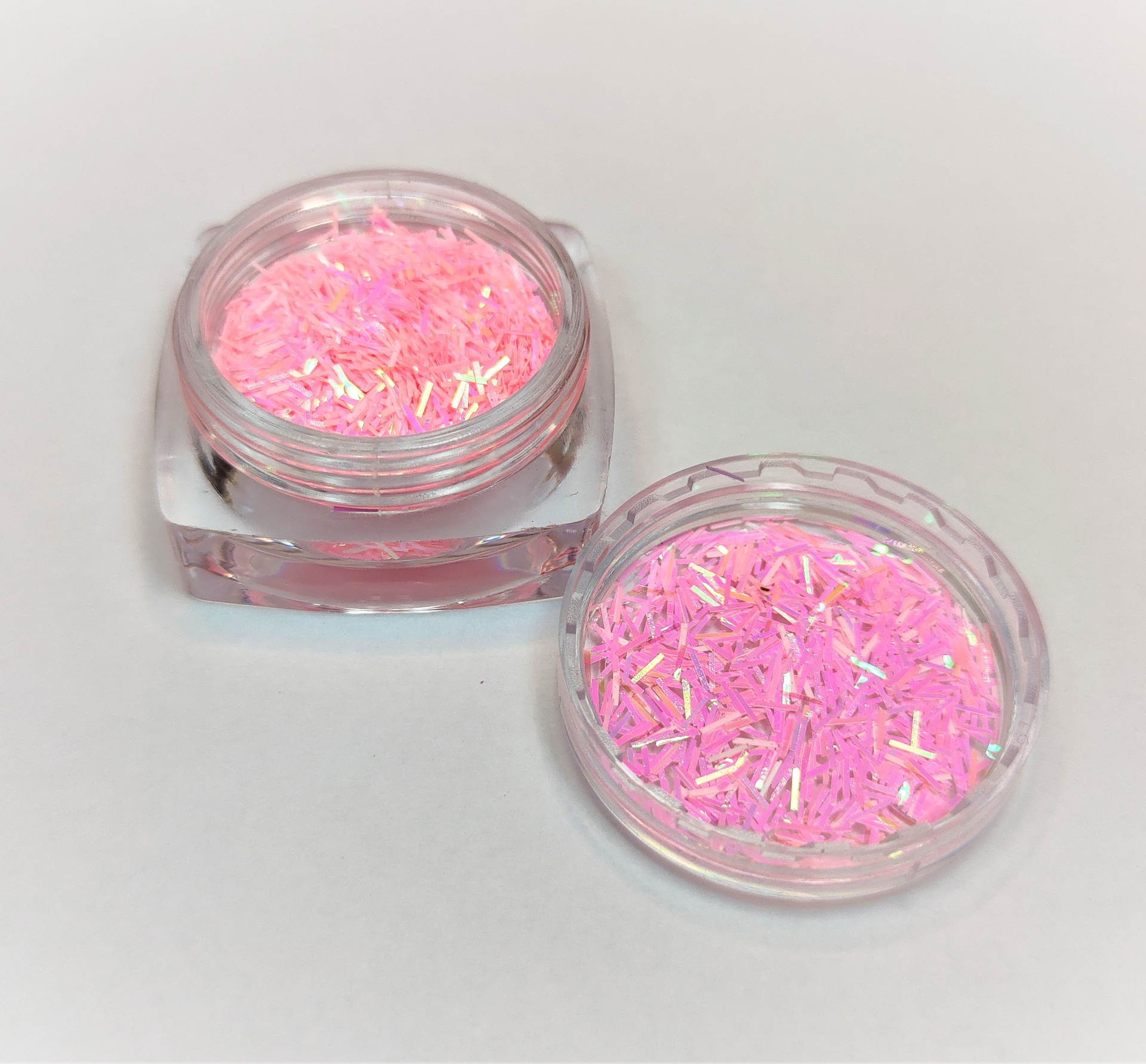 Pote transparente com glitter rosa e tampa ao lado sobre fundo branco