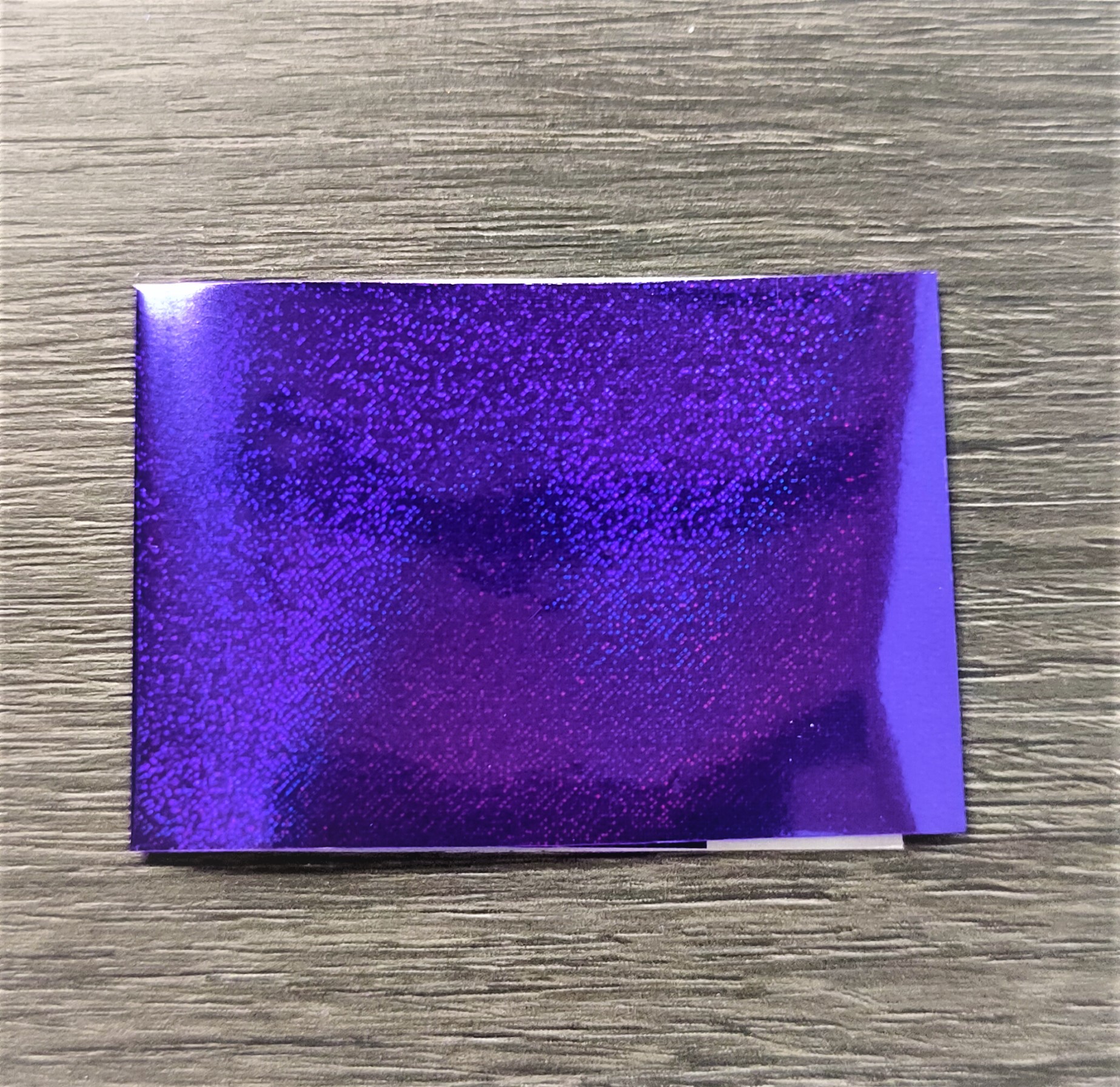 Papel holográfico roxo brilhante sobre superfície de madeira clara