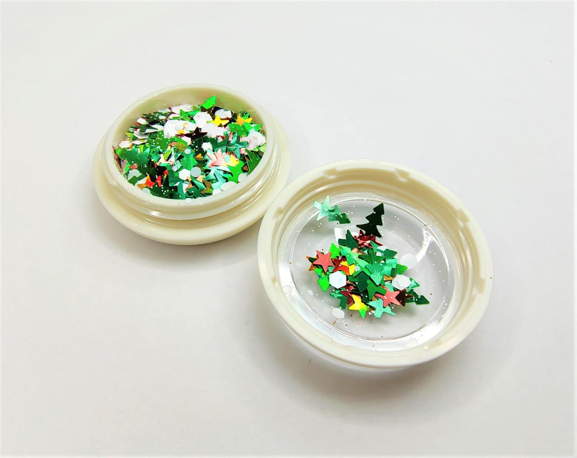 Dois recipientes plásticos com confetis coloridos em forma de estrelas e árvores de Natal