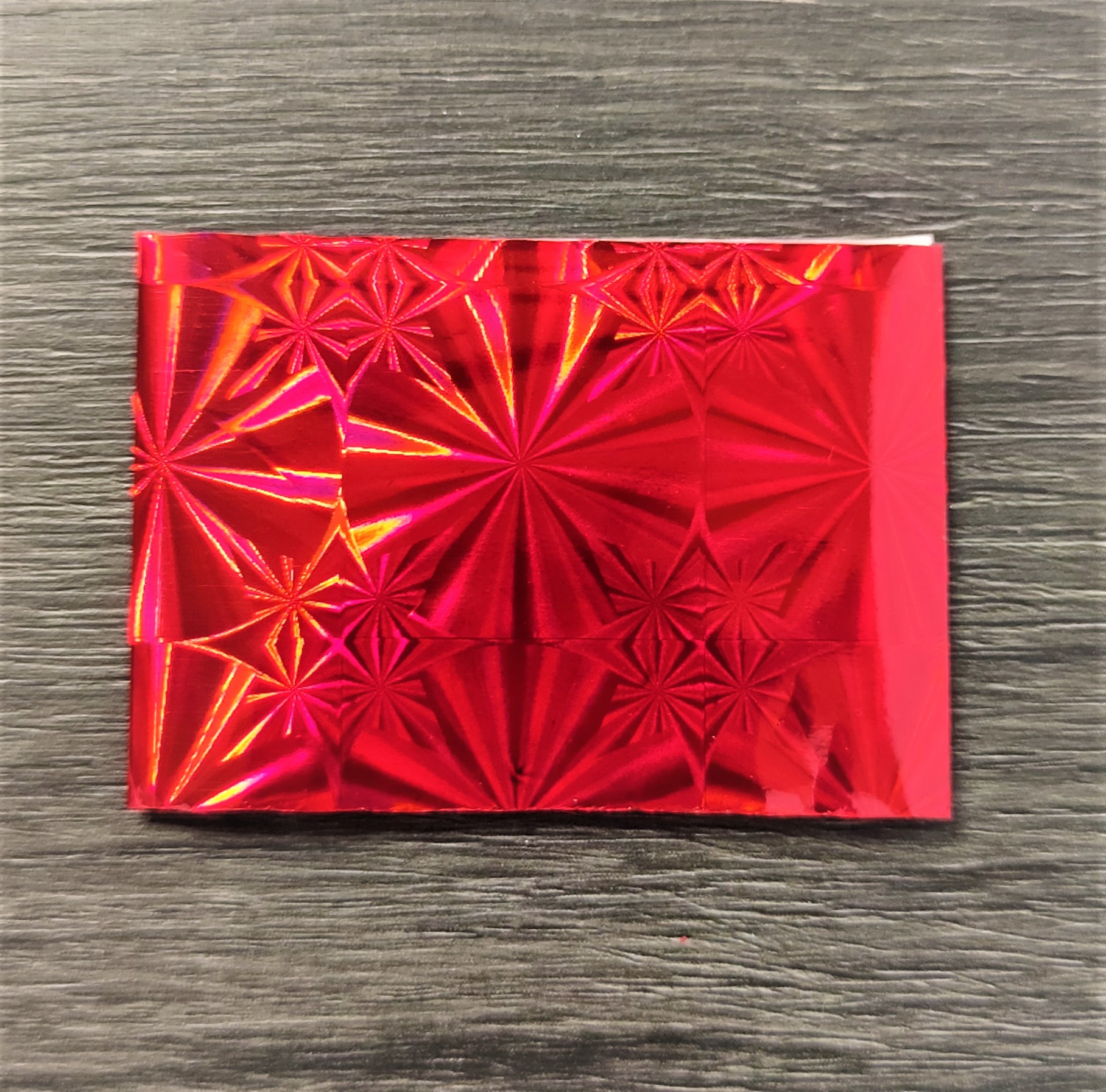 Papel decorativo vermelho metálico com padrão em relevo sobre madeira cinza