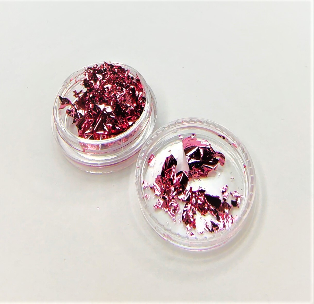 Duas embalagens transparentes com pedaços metálicos cor de rosa.