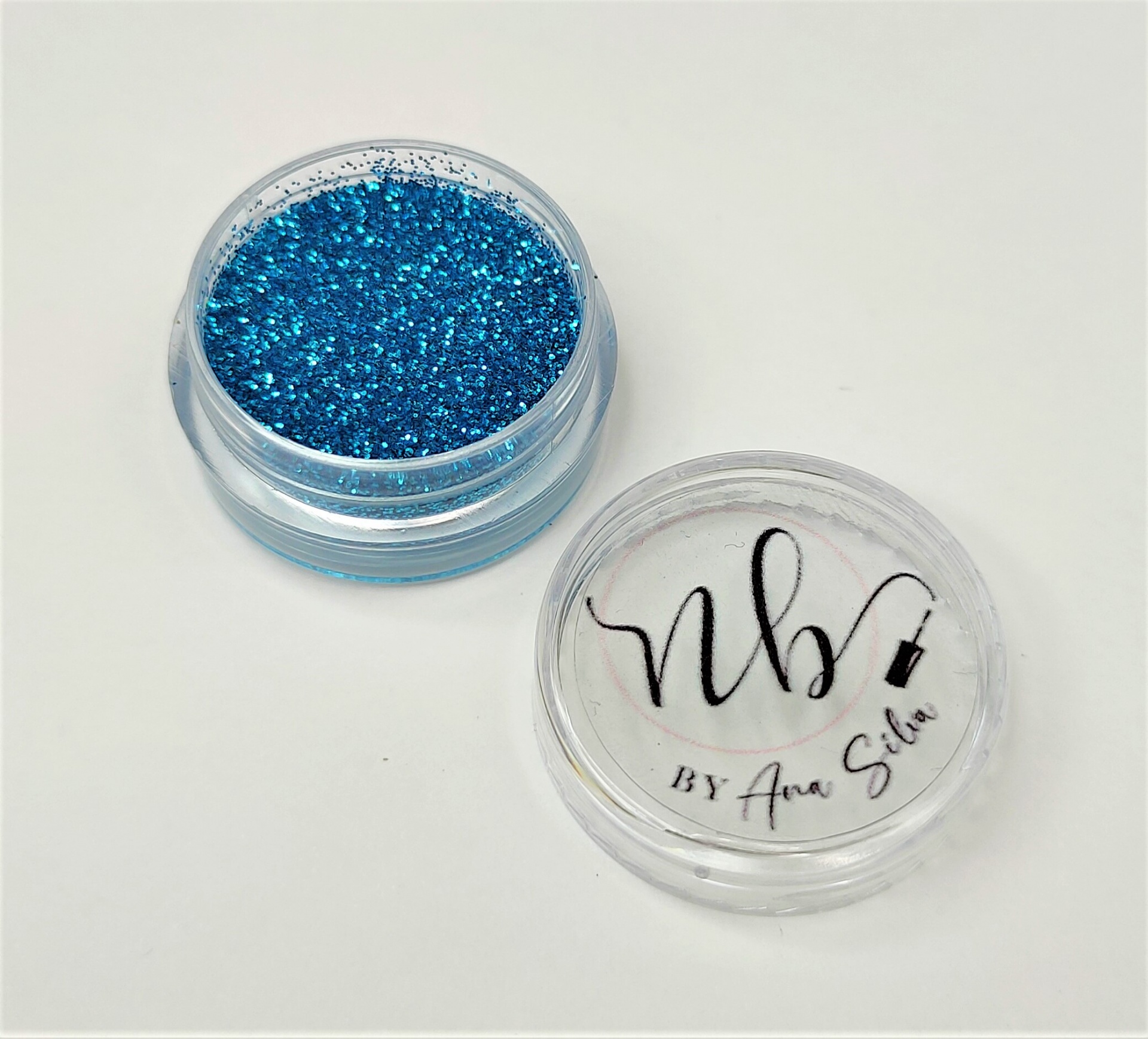Recipiente plástico com pó brilhante azul e tampa com texto 'nb by Ana Silva'
