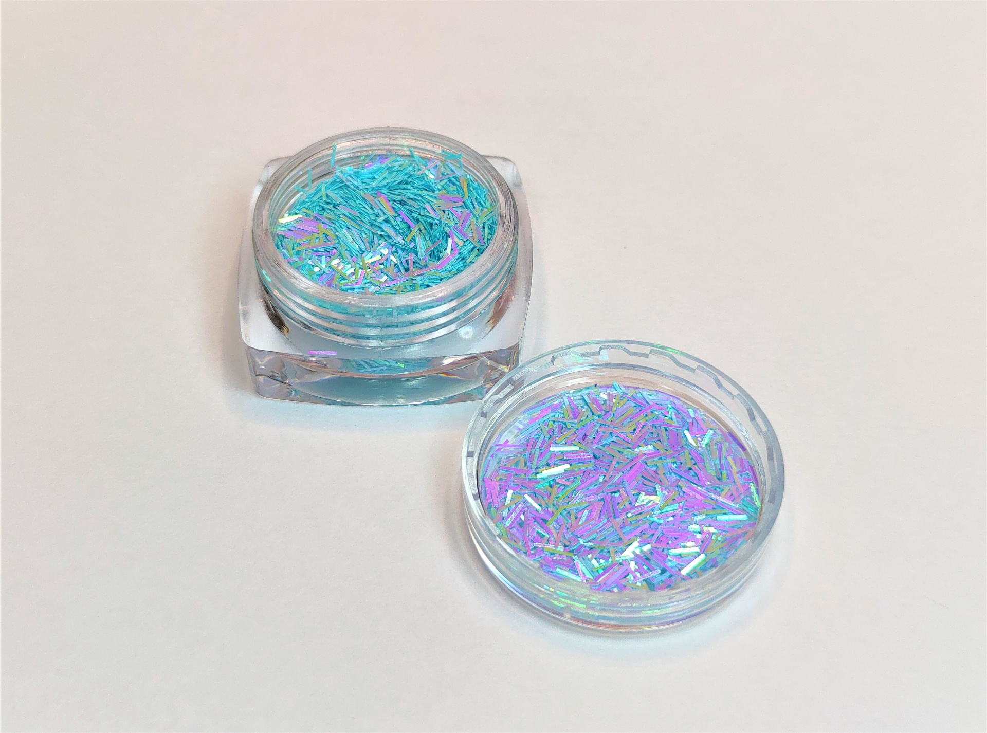 Frasco com glitter holográfico azul e roxo aberto sobre superfície branca