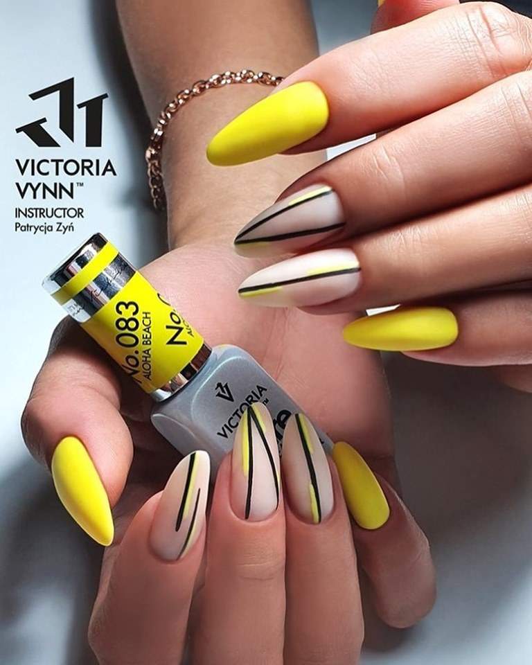 Unhas decoradas em gel amarelo e nude com linhas finas pretas e amarelas, com frasco da marca Victoria Vynn.