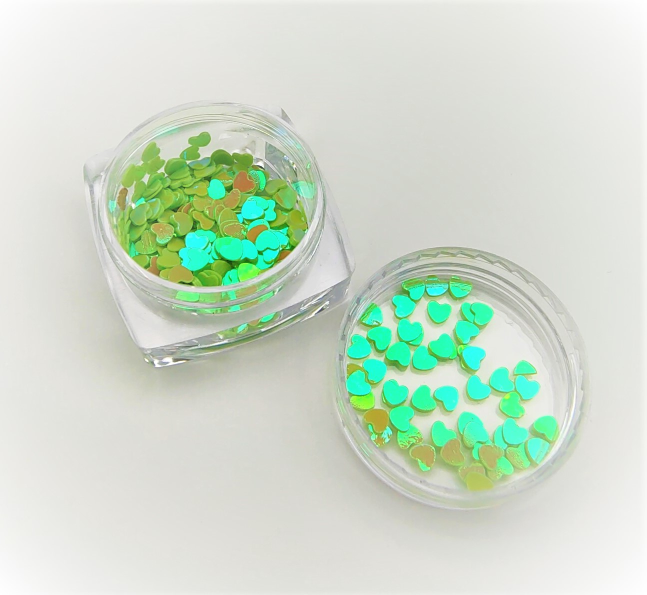 Dois frascos pequenos com glitter em forma de corações verdes holográficos