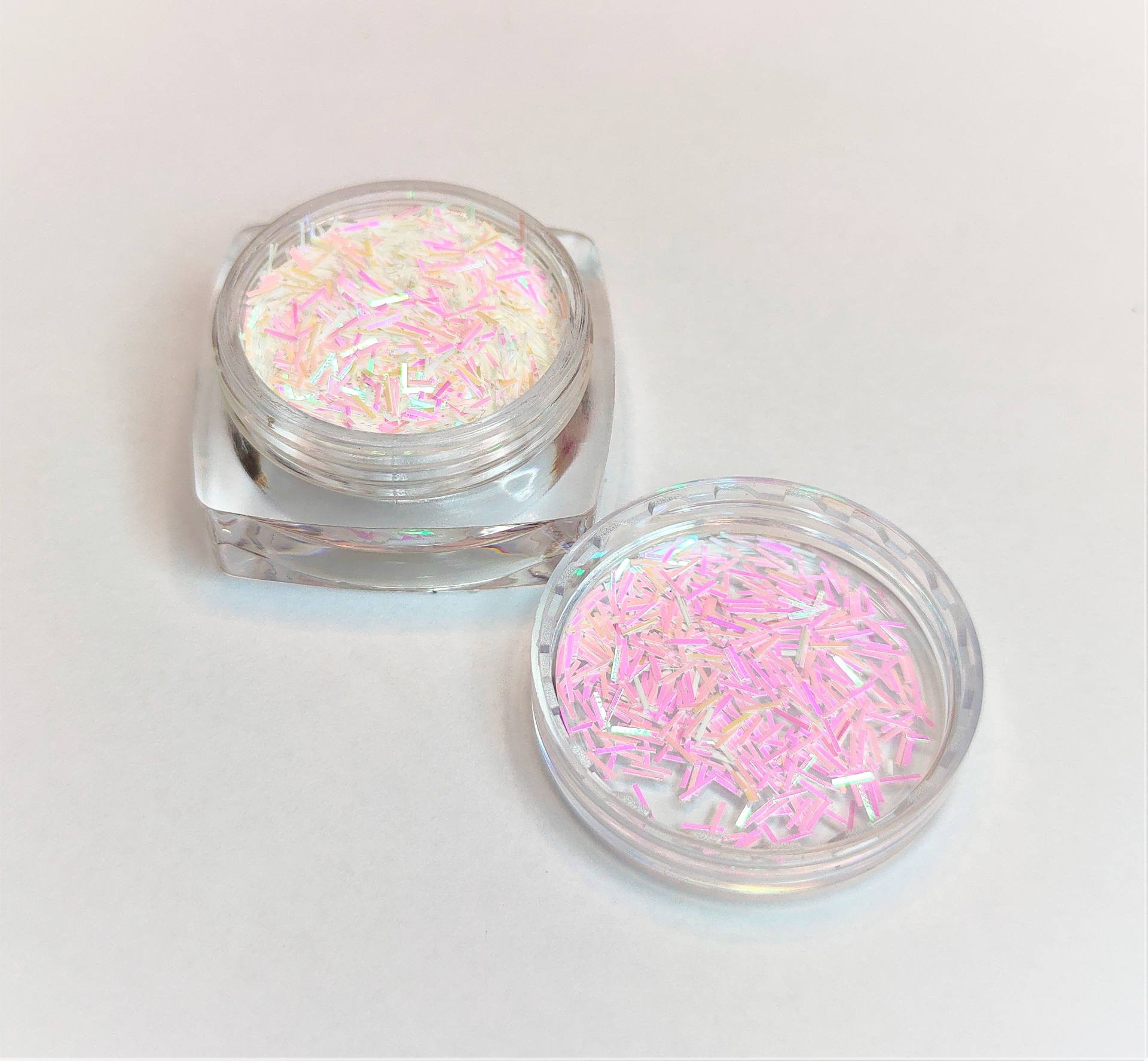 Frasco de plástico transparente com glitter branco com reflexos rosa e lilás sobre superfície branca