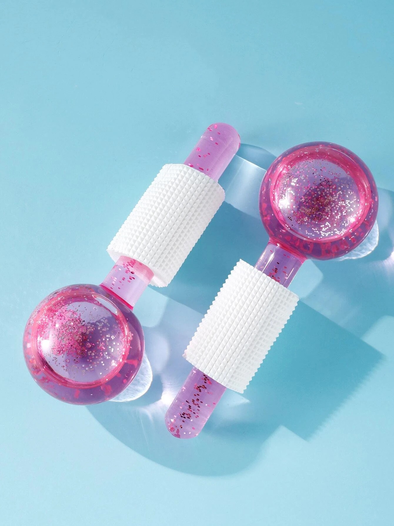 Dois massajadores rosas com purpurina e pega branca sobre fundo azul