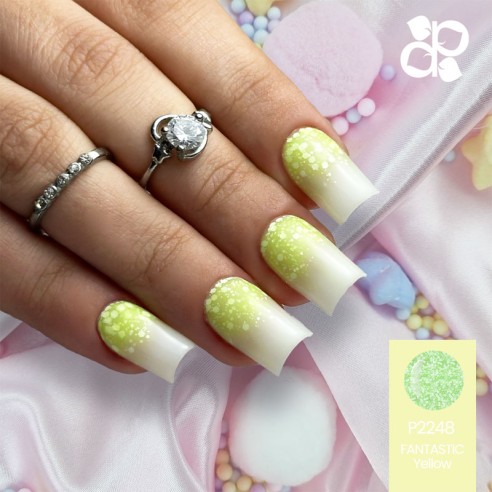 Unhas artificiais amarelas e brancas com efeito brilhante e bolinhas, mão com anel prateado, fundo de tecido rosa acetinado