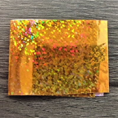 Embalagem metálica dourada holográfica numa superfície cinzenta de padrão madeira