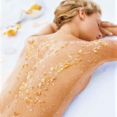 Mulher deitada com esfoliante corporal nas costas num ambiente branco