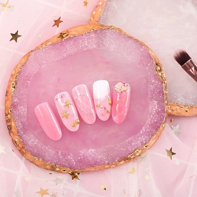 Unhas postiças decorativas em rosa com detalhes dourados e pérolas sobre base de pedra rosa