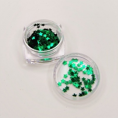 Purpurina em forma de estrelas verdes num recipiente de plástico transparente aberto sobre fundo branco.