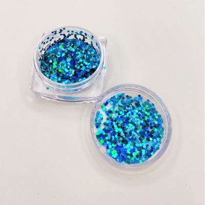Dois frascos pequenos transparentes com glitter azul verde prateado sobre superfície branca