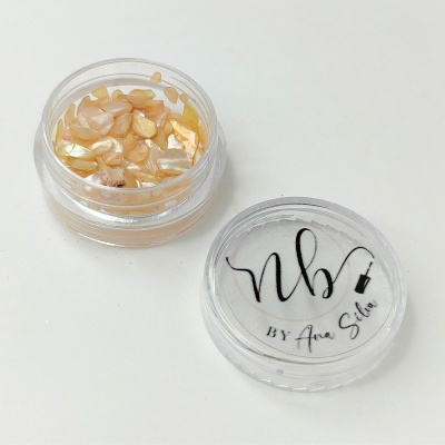 Pote transparente com fragmentos bege e dourados e tampa com texto nb BY Ana Silva