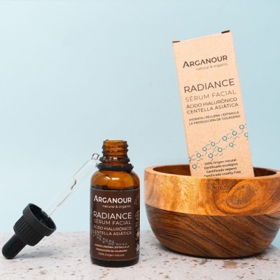 Frasco de sérum facial Arganour Radiance e embalagem de cartão ao lado de pote de madeira