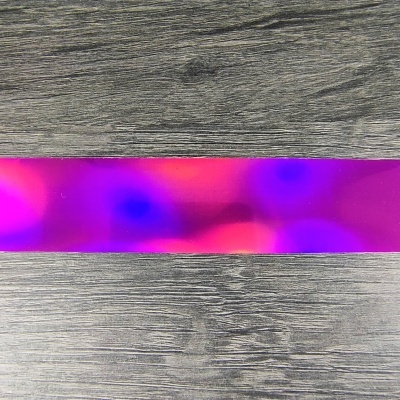 Fita plástica holográfica rosa e roxa sobre superfície cinza imitando madeira