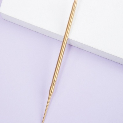 Ferramenta metálica dourada com ponta de pente e ponta fina sobre fundo branco e lilás