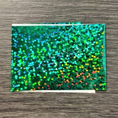 Cartão verde holográfico com bolinhas coloridas sobre mesa de madeira cinzenta