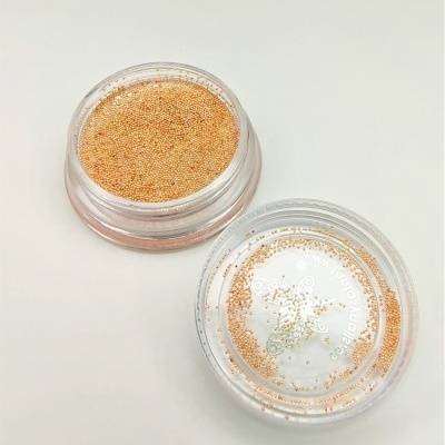 Pote transparente com microesferas douradas e tampa ao lado