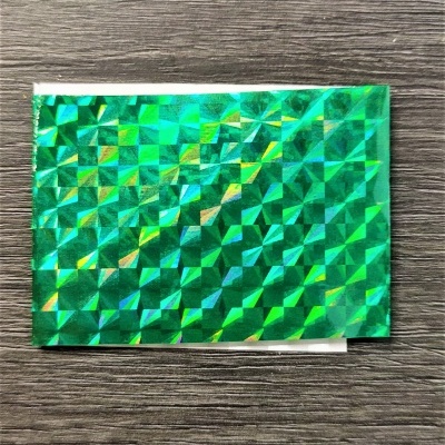 Envelope pequeno de papel holográfico verde com padrão geométrico em madeira escura