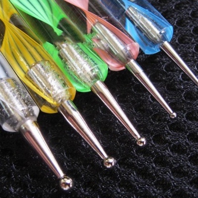 Ferramentas coloridas para decoração de unhas com pontas metálicas sobre fundo preto