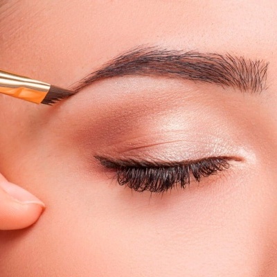 Olho fechado com sombra bege e sobrancelha sendo delineada com pincel dourado