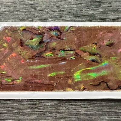 Fita adesiva decorativa com padrão iridescente e relevo sobre madeira cinzenta