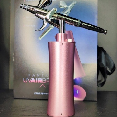 Aerógrafo metálico com base rosa diante de caixa com texto UV AIRBRUSH