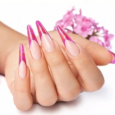 Mão com unhas artificiais transparentes e rosas, fundo com flores cor-de-rosa