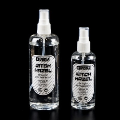 Duas garrafas transparentes de spray com extrato de hamamélis, rótulos brancos e pretos, em fundo preto