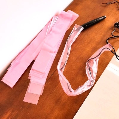 Fita elástica rosa, fita plástica transparente e caneta preta sobre mesa de madeira