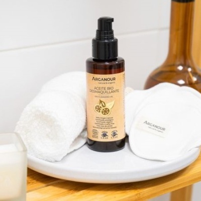Frasco de cosmético Arganour com toalhas e discos de algodão em prateleira de madeira