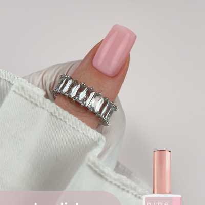 Frasco de verniz gel rosa claro com unha pintada da mesma cor e anel de pedras brilhantes