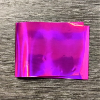 Folha de material plástico metálico rosa com efeito iridescente sobre superfície de madeira cinza