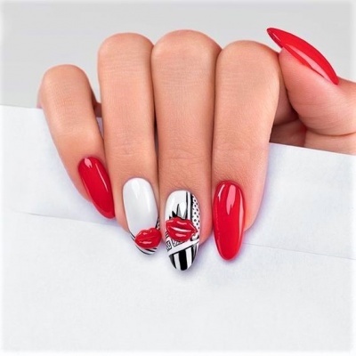 Unhas artificiais decoradas com verniz vermelho brilhante e estampas de lábios vermelhos sobre fundo branco com padrões pretos.