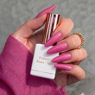 Mão com unhas rosas segurando frasco branco de produto para unhas com tampa dourada