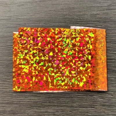 Folha holográfica laranja refletiva sobre superfície de madeira escura