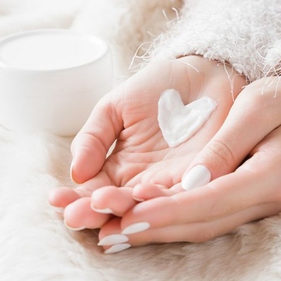 Mãos femininas com creme branco em forma de coração, frasco de creme branco e superfície peluda