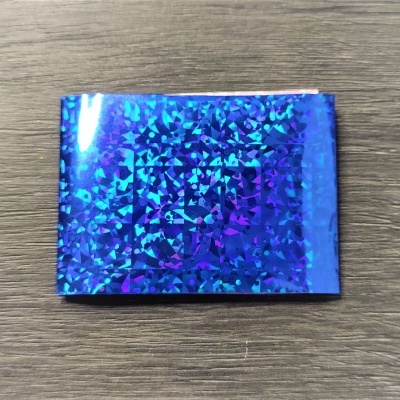 Folha holográfica retangular azul e roxa sobre madeira cinzenta