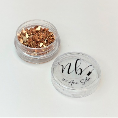 Pote transparente com pedaços metálicos dourados e tampa com texto 'nb BY Ana Silva'.