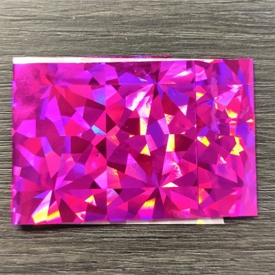 Papel holográfico rosa com padrão facetado sobre madeira cinzenta