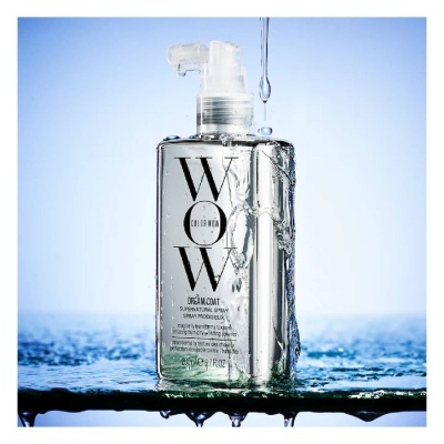 Frasco transparente de spray com tampa branca e texto preto sobre fundo azul com gotas de água