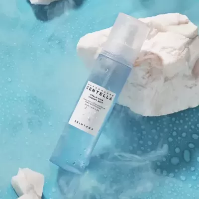 Frasco azul claro de toner cosmético SKINFOOD sobre superfície azul com gotas de água e pedras brancas